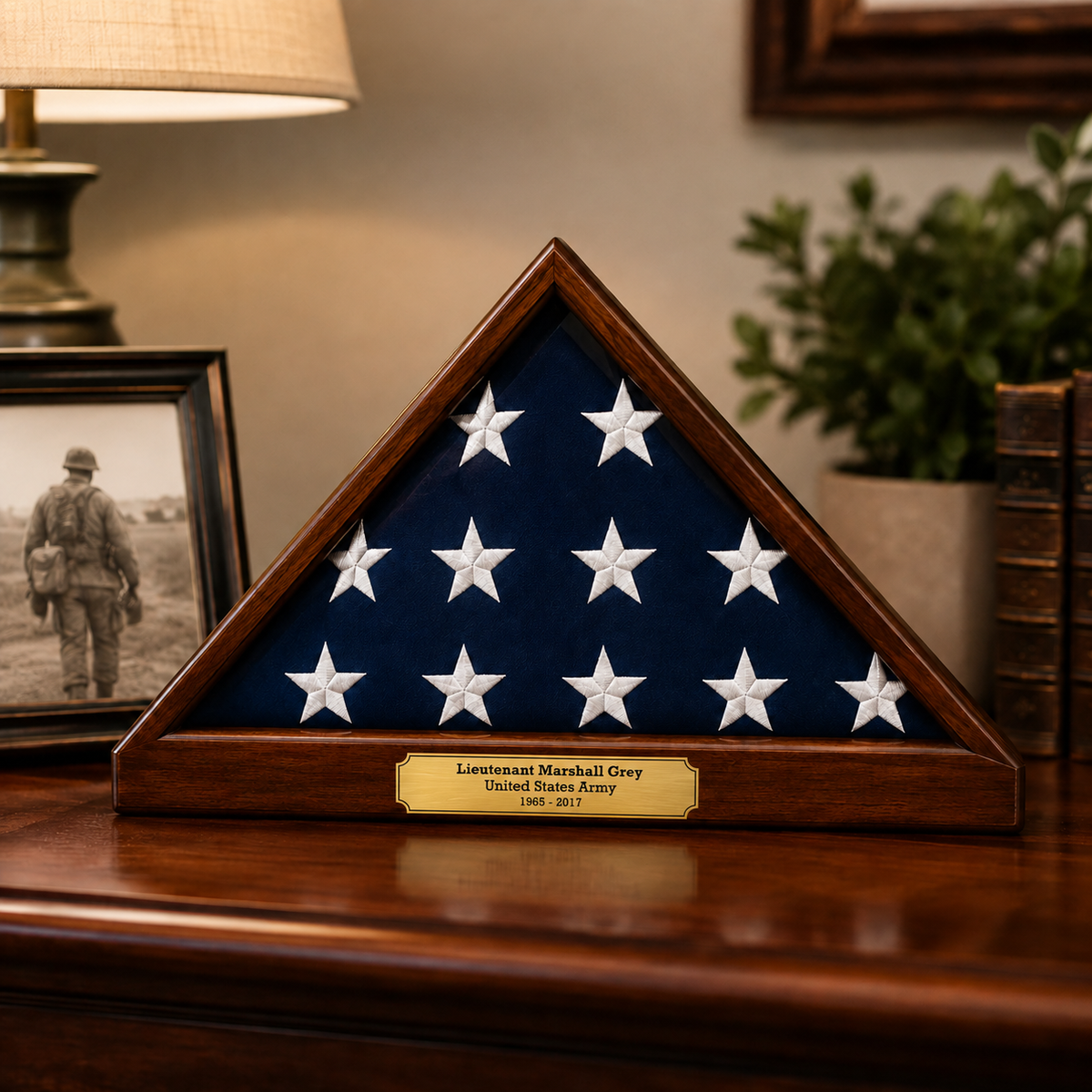 A triangular wooden display case containing a folded American flag with white stars on a dark blue field, placed on a polished wooden surface. A brass plaque at the base reads 'Lieutenant Marshall Grey United States Army 1943 - 2021.